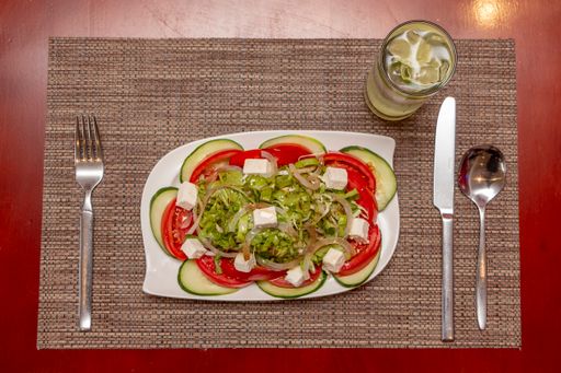 An overhead shot of fresh vegetable salad with cheese on a white ceramic plate