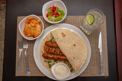 A top view of Shish taouk, bread, sesame paste , and cutlery on a white plate on a gray table