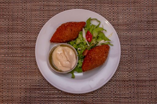A top view of tasty cutlets with fresh greens and a dip on a plate