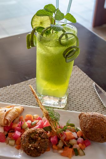 A vertical shot of cutlets and salsa on a plate beside a green smoothie