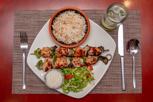 A top view of Shish taouk, rice, sesame paste, and cutlery on a white plate on a red table