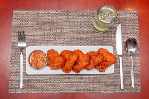 An overhead shot of appetizing chicken wings and sauce on white platter served at a restaurant