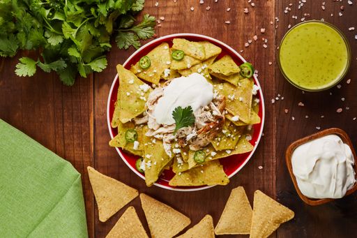 A top view of a spicy dish with potato chips and sour cream on a table