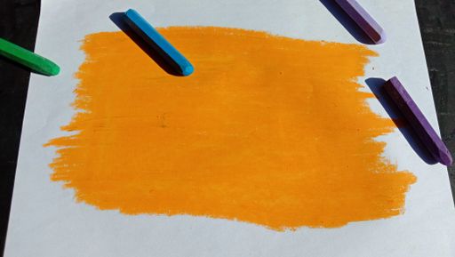 A picture painted with an orange crayon on the paper with other colorful crayons on it