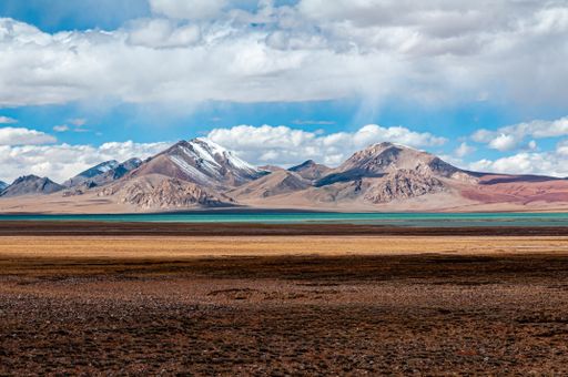 A colofrul landscape with brown shore, blue water and snowy mountains on the horizon
