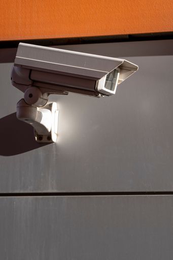 Security camera mounted on a modern building facade with orange and gray tones, highlighting urban surveillance.