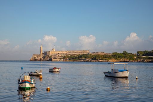 A scenic shot of fishing boats in the bay of Havana with Castillo del Morro in the background