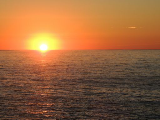 A stunning sunset over the ocean with vibrant orange hues and a calm sea reflecting the sunlight.