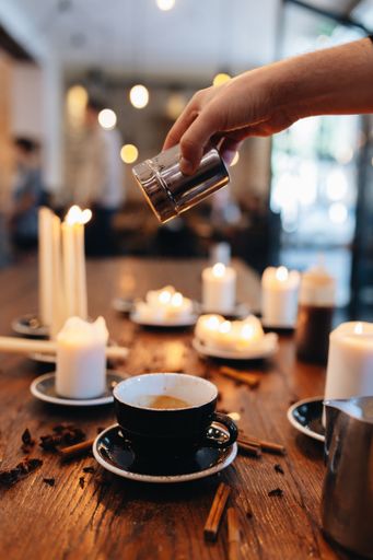 A cozy coffee shop setting with syrup bottles and lit candles on a wooden table.