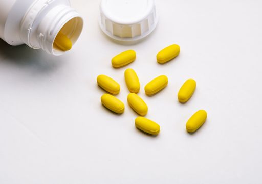 A top view closeup of yellow pills from the white bottle on a white table