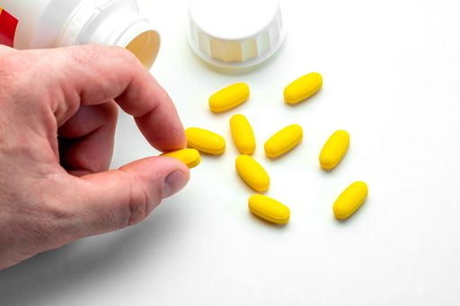 A top view closeup of yellow pills from the white bottle on a white table