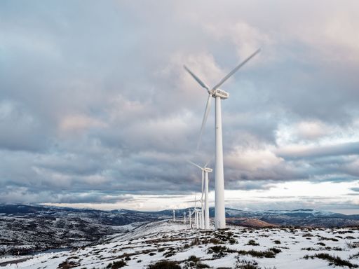 Wind turbines on a snowy mountain landscape under a dramatic cloudy sky, showcasing renewable energy in a winter setting.
