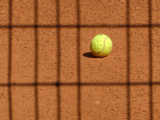 A closeup shot of a yellow tennis ball on a tennis clay with checked shadows