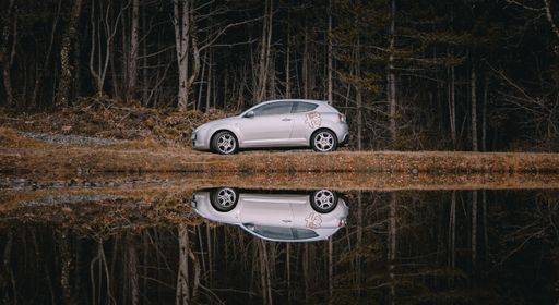 A closeup shot of an  Alfa Romeo MITO car driving near the lake and its reflection on the water