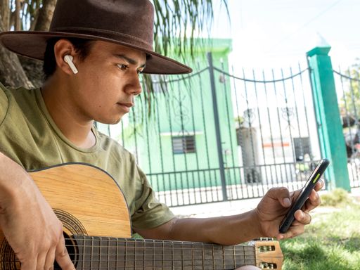 A Hispanic musician playing guitar for using a phone in a park