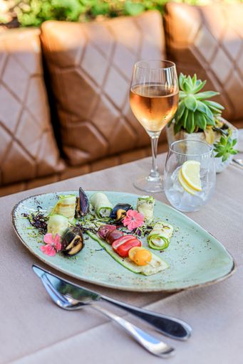 A close up of a green ceramic big plate with small colored tomatoes, glass of wine and cutlery