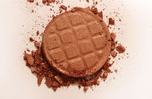 Close-up of a broken bronzer powder compact on a white background, showcasing texture and color.