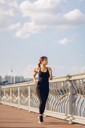 A slim South Korean girl in black sportswear is running on the embankment