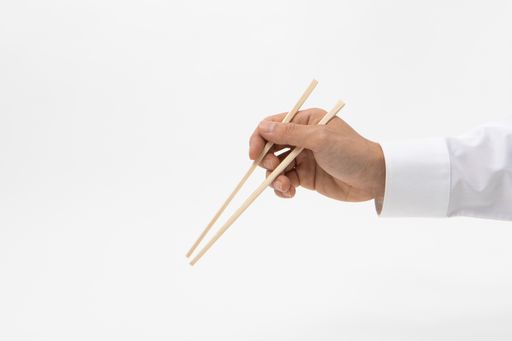 A closeup shot of a person's hand holding a pair of wooden chopsticks on a white background