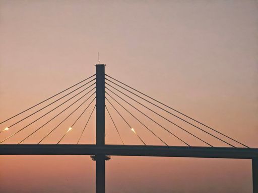 A silhouette of a cable-stayed bridge against a warm sunset sky, showcasing architectural elegance