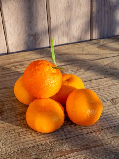 A pile of fresh oranges with a green leaf on rustic wooden table in natural light.