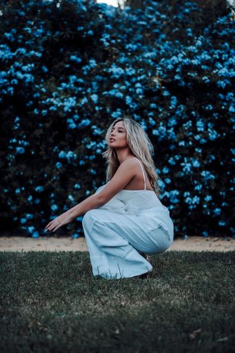 A young woman squatted elegantly against a backdrop of blue floral plants.
