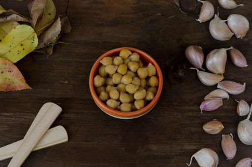 A top view shot of chickpeas on a wooden table decorated with garlic, leaves and wooden spoons, hummus ingredients
