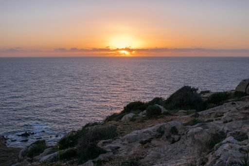 Peaceful beautiful sunset with few clouds along the coast of Qrendi, Malta, on top of cliffs with garigue vegetation and the sun setting in horizon.
