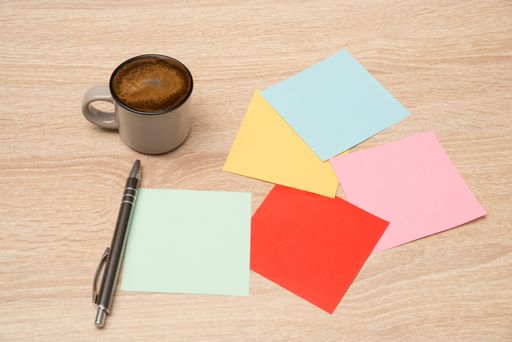 A cup of coffee, colored paper notes, and a pen on a wooden surface
