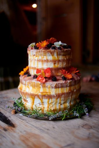 A closeup shot of a wedding cake decorated with blackberries and flowers on the wooden table