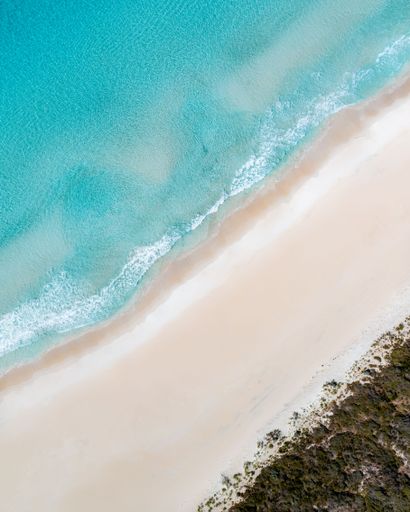 Aerial view of a pristine beach with turquoise waters and white sand, showcasing natural beauty and tranquility.