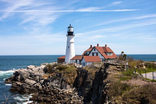 Scenic view of Portland Head Light lighthouse on a rocky coastline under a clear blue sky in Cape Elizabeth, Maine.