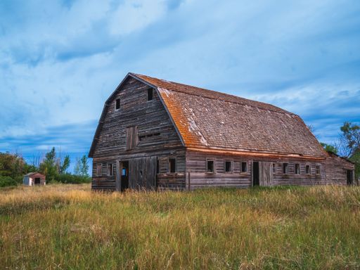 A rustic wooden barn stands in a grassy field under a vibrant blue sky.