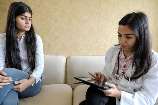 Two young Indian females having a discussion while sitting on the sofa at home