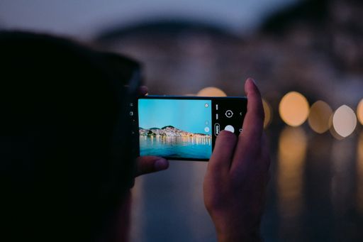 A selective focus shot of hands holding a smartphone taking a photo of a lake in the evening