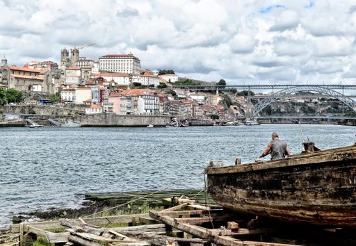 A person working in his boat over the river in Oporto, Portugal with houses on the other side.