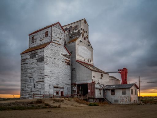 An abandoned grain elevator stands against a moody sky in a rural landscape at sunset, showcasing rustic architecture and history.