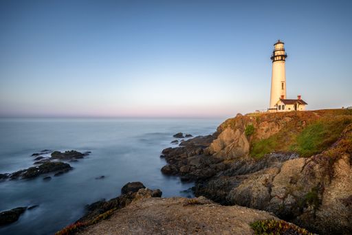 Scenic view of Pigeon Point Lighthouse at sunset with rocky coastline and calm ocean in California.