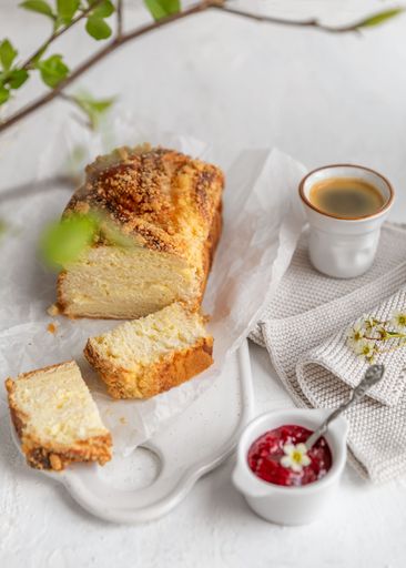 A freshly baked loaf of bread with slices, served with a cup of coffee and raspberry jam on a white background.