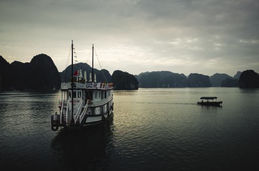 A beautiful shot of the white ship and a boat in the calm sea with cliffs in the background