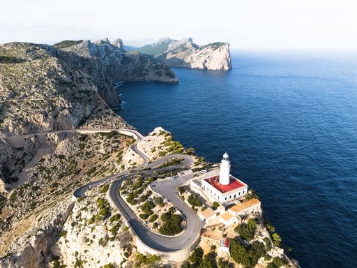 An aerial view of Cap de Formentor lighthouse on Mallorca's rugged coastline, with winding roads