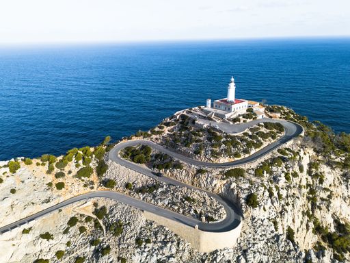 An aerial view of Cap de Formentor lighthouse on a cliff with winding road in Mallorca, Spain.