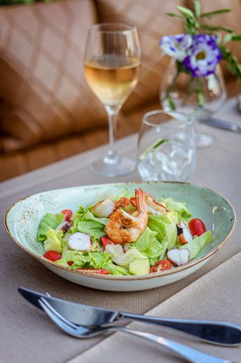 A vertical shot of fresh salad with cutlery, a glass of wine and flowers on the table