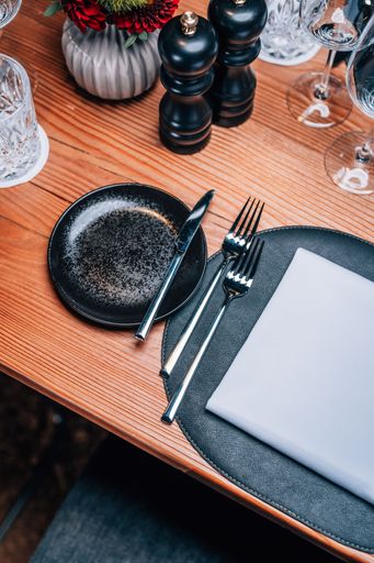 Elegant table setting with black plate, silverware, and crystal glasses on a wooden surface.