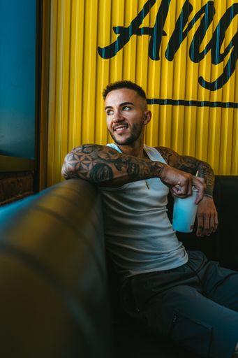 A happy tattooed male sitting in the cafe and drinking a refreshing drink