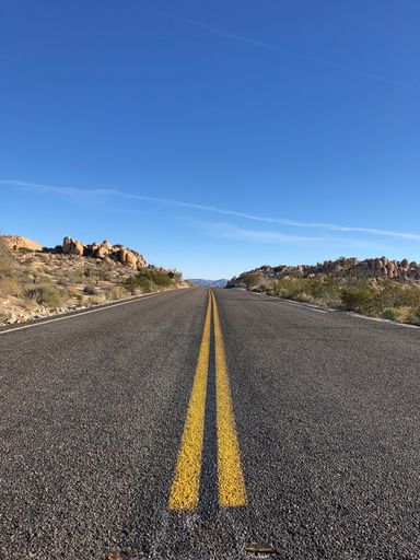 An asphalt road with yellow lines under a clear blue sky