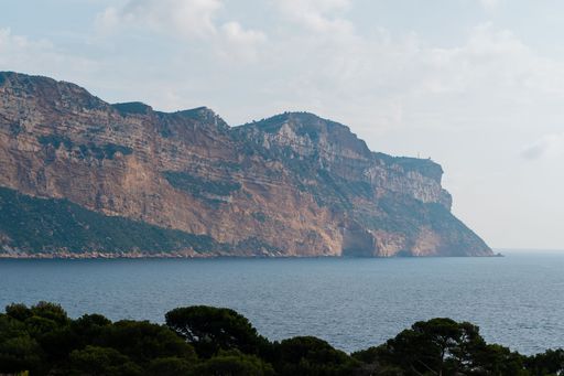 Scenic view of a rocky coastal cliff with lush greenery and calm sea under a partly cloudy sky.