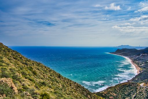 An aerial shot of a scenic coast and blue ocean water under a cloudy sky