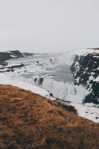 A breathtaking view of Gullfoss waterfall in Iceland, surrounded by snow and rugged terrain under an overcast sky.