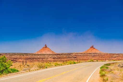 Scenic view of the iconic Bears Ears Buttes under a clear blue sky in Utah, with a winding road leading towards the formations.